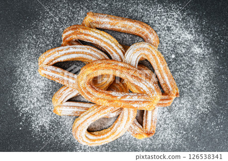 Traditional spanish dessert churros, fried dough pastry dusted with powdered sugar, black background Traditional spanish dessert churros, fried dough pastry dusted with powdered sugar, black background 126538341