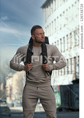 muscular man stands confidently on a city street wearing casual athletic clothing and carrying a backpack. He exudes determination and fitness ready for the next challenge. muscular man stands confidently on a city street wearing casual athletic clothing and carrying a backpack. He exudes determination and fitness ready for the next challenge. 126538720
