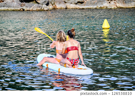 Two women, mother and daughter, paddleboarding on the beautiful beach of Cala en Blanes, Menorca, Balearic Islands 126538810