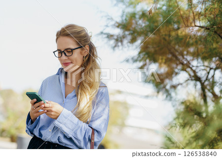 A Young Woman Glamorously Texting Outdoors While Wearing Stylish Glasses in Nature A Young Woman Glamorously Texting Outdoors While Wearing Stylish Glasses in Nature 126538840