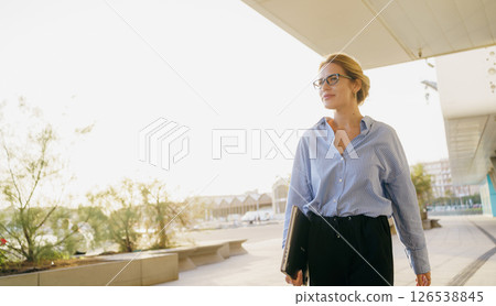 A confident businesswoman is walking outdoors in an urban city environment during the daytime A confident businesswoman is walking outdoors in an urban city environment during the daytime 126538845