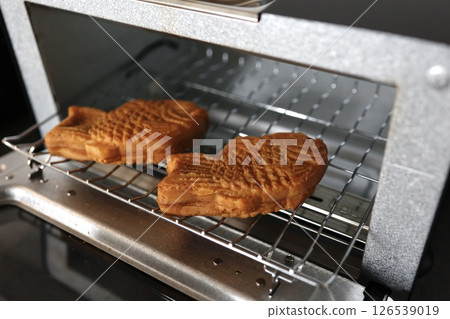 Two taiyaki are being cooked in a toaster oven. Two taiyaki are being cooked in a toaster oven. 126539019