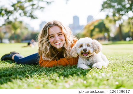 A woman and her dog are laying on the grass in a park 126539617