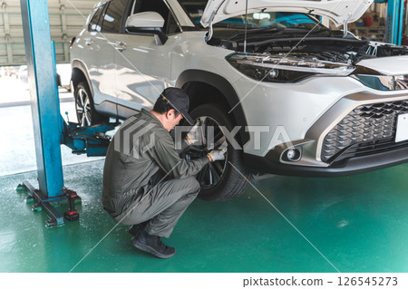 A male mechanic changing a tire on a lifted car A male mechanic changing a tire on a lifted car 126545273
