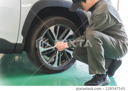 A male mechanic changing a tire on a lifted car 126547143