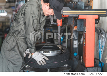 A male mechanic/service technician changing tires using a tire changer A male mechanic/service technician changing tires using a tire changer 126547226