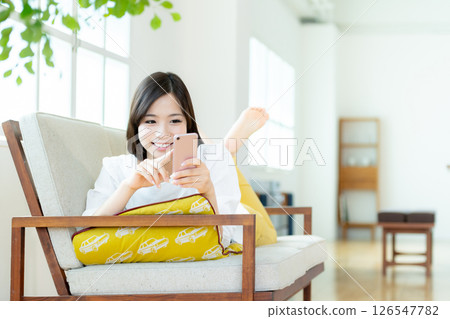 A young woman operating a smartphone in the living room 126547782