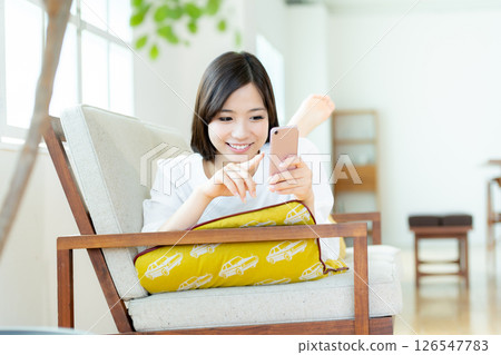 A young woman operating a smartphone in the living room 126547783