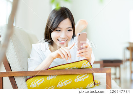 A young woman operating a smartphone in the living room 126547784