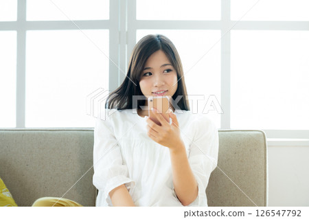 A young woman operating a smartphone in the living room 126547792