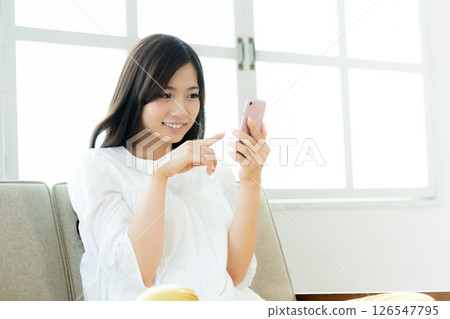 A young woman operating a smartphone in the living room A young woman operating a smartphone in the living room 126547795