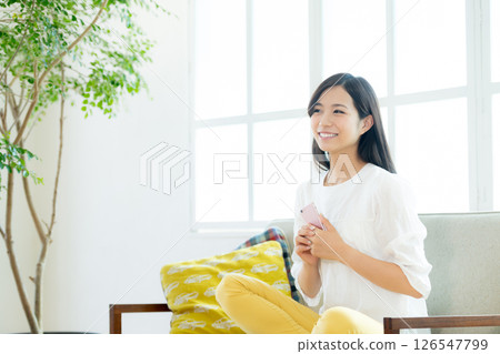 一個年輕的女人,在客廳裡操作智能手機 一個年輕的女人,在客廳裡操作智能手機 126547799