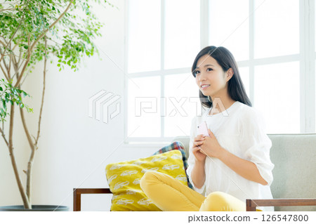 一個年輕的女人,在客廳裡操作智能手機 一個年輕的女人,在客廳裡操作智能手機 126547800