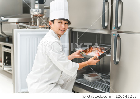 A male chef in a chef's coat taking ingredients out of the refrigerator 126549213