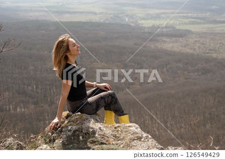 Woman Relaxation Mountain: Woman sitting peacefully atop mountain rocks, enjoying nature on a bright day. 126549429