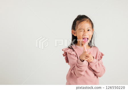 Cheerful Asian young kid girl excitedly makes two gun finger gesture to the camera with a friendly and cheeky expression. Isolated on white background, kindergarten child exudes positivity and joy 126550220