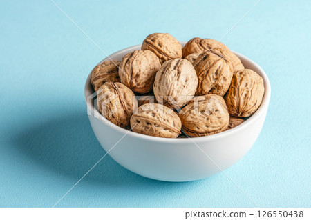 A white bowl filled with walnuts sits on a light blue background.  126550438