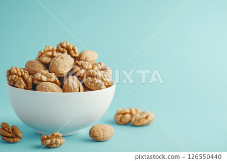A white bowl filled with walnuts sits on a light blue background.  126550440