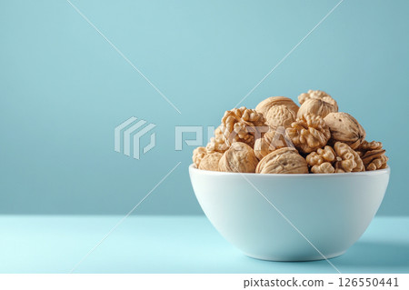 A white bowl filled with walnuts sits on a light blue background.  126550441
