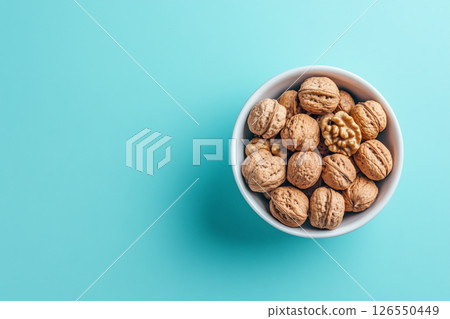 A white bowl filled with walnuts sits on a light blue background. A white bowl filled with walnuts sits on a light blue background. 126550449