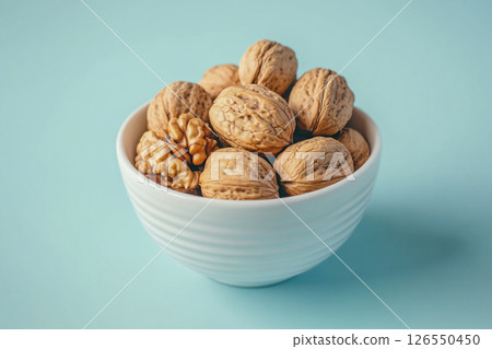 A white bowl filled with walnuts sits on a light blue background.  126550450