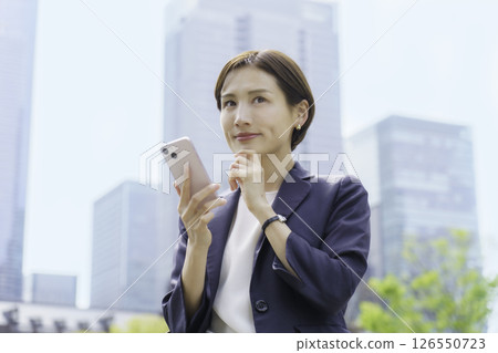 東京車站前一位年輕女商人拿著智慧型手機 東京車站前一位年輕女商人拿著智慧型手機 126550723
