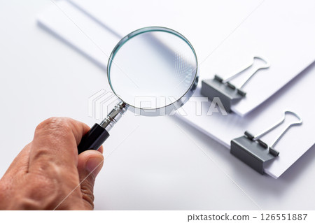 Hand holding a magnifying glass and a document clipped 126551887