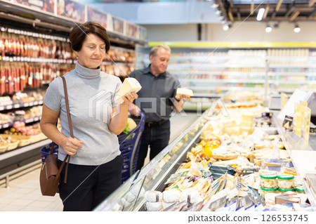 Elderly female customer looking around in dairy section of supermarket Elderly female customer looking around in dairy section of supermarket 126553745