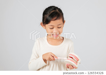 Dentist explains tooth loss to smiling girl holding toothbrush and teeth model. Asian kid with gap learns about milk teeth, dental care, and good hygiene. isolated white background 126554326