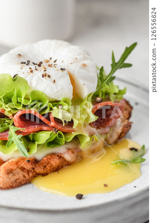 Toasted bread with poached egg, salad, cheese and ham on a plate on white kitchen background close up. Healthy breakfast, diet food 126556824