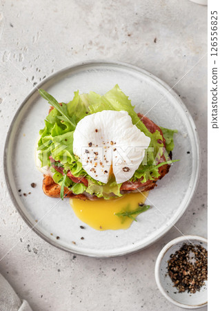 Toasted bread with poached egg, salad, cheese and ham on a plate on white kitchen background. Healthy breakfast, diet food 126556825