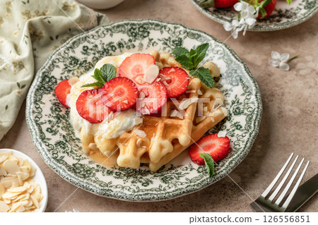Homemade belgian waffles with strawberries, whipped cream and honey. Served on a rustic plate with spring flowers Homemade belgian waffles with strawberries, whipped cream and honey. Served on a rustic plate with spring flowers 126556851