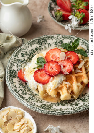 Homemade belgian waffles with strawberries, whipped cream and honey close up. Served on a rustic plate with spring flowers 126556852