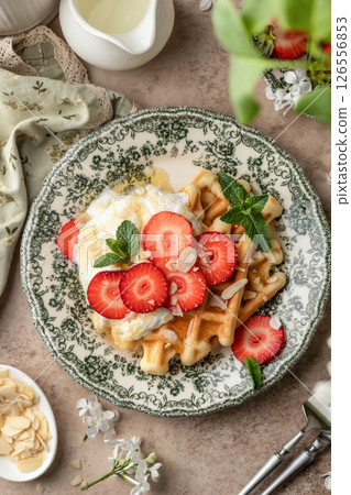 Homemade belgian waffles with strawberries, whipped cream and honey top view. Served on a rustic plate with spring flowers 126556853