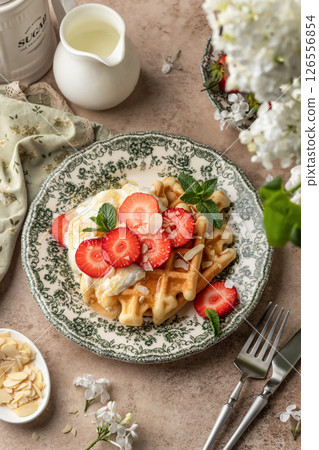 Homemade belgian waffles with strawberries, whipped cream and honey. Served on a rustic plate with spring flowers 126556854