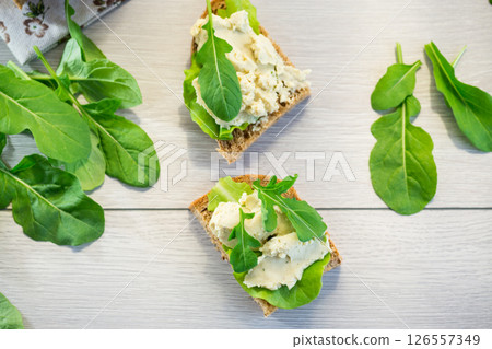 Appetizing sandwich with greens and fish spread on a light wooden table Appetizing sandwich with greens and fish spread on a light wooden table 126557349