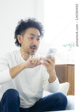 A man holding his head while looking at his smartphone 126560492