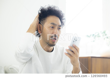 A man holding his head while looking at his smartphone A man holding his head while looking at his smartphone 126560493
