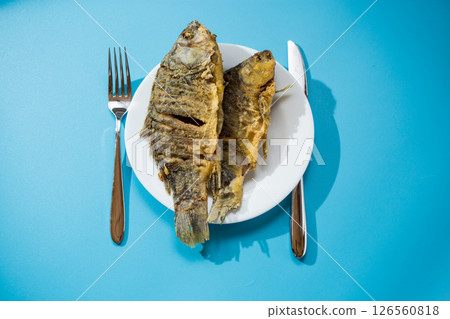Fried crucian carp with a crispy golden crust on a white plate 126560818