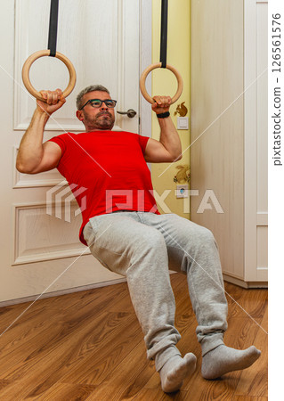 Man practices strength training with gymnastic rings indoors Man practices strength training with gymnastic rings indoors 126561576