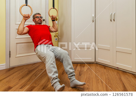Man performs pull-ups on gymnastic rings indoors Man performs pull-ups on gymnastic rings indoors 126561578