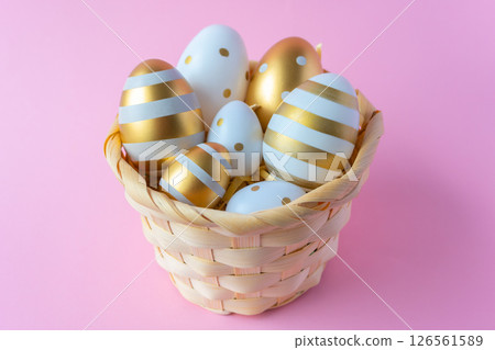 Gold Easter eggs in woven natural basket on a pink background. Easter concept for greeting card. Gold Easter eggs in woven natural basket on a pink background. Easter concept for greeting card. 126561589