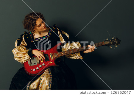 Portrait of a young adult woman playing classical music on electric guitar and dressed in a medieval dress 126562047