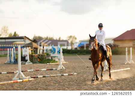 Woman rider jockey in helmet and white uniform preparing horse racing Woman rider jockey in helmet and white uniform preparing horse racing 126562055