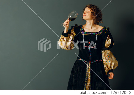Young adult woman dressed in a medieval dress holding a glass of wine and drinking a red wine Young adult woman dressed in a medieval dress holding a glass of wine and drinking a red wine 126562060