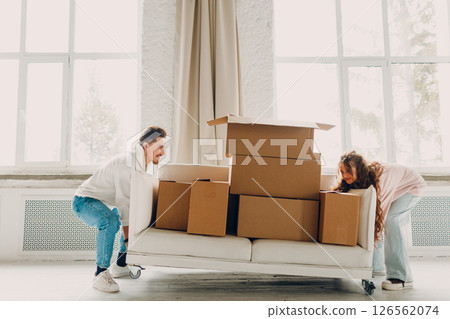 Happy young family couple man and woman push sofa with cardboard boxes in new home. Moving delivery concept. Happy young family couple man and woman push sofa with cardboard boxes in new home. Moving delivery concept. 126562074