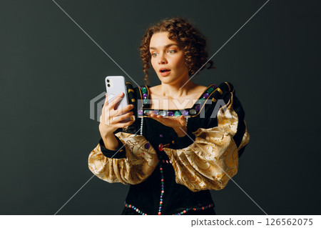 Portrait of a young aristocratic woman doing photo selfie with mobile phone and dressed in a medieval dress Portrait of a young aristocratic woman doing photo selfie with mobile phone and dressed in a medieval dress 126562075