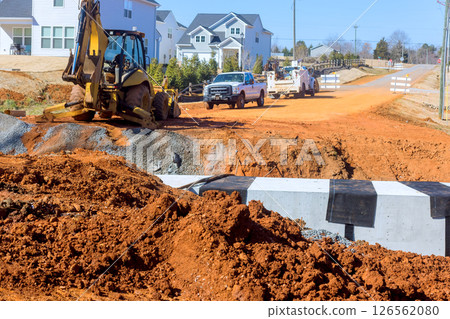 Heavy machinery operates on rural road, repairing surface while vehicles await passage at works zone progress. 126562080