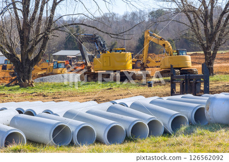 Heavy machinery working on infrastructure development construction site surrounded by concrete pipes under works zone 126562092