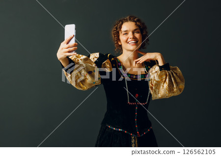 Portrait of a young aristocratic woman holding mobile phone dressed in a medieval dress on dark background Portrait of a young aristocratic woman holding mobile phone dressed in a medieval dress on dark background 126562105